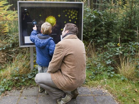 Een vader kijkt met zijn zoontje naar een bord met uitleg langs het melkwegpad.
