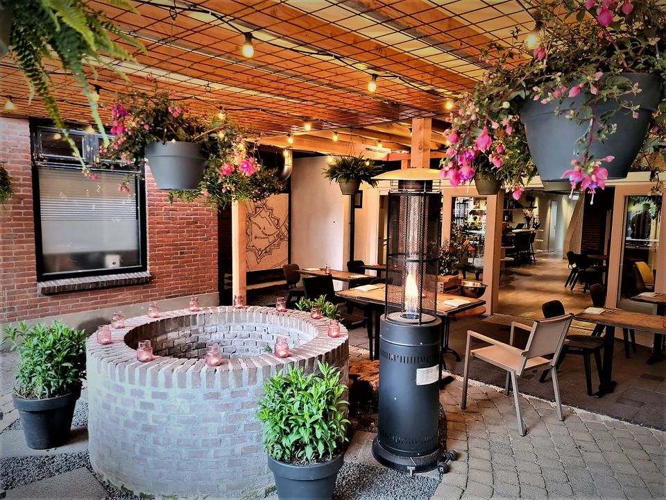 Sfeervolle binnentuin met terras en heaters bij restaurant De Woerdenaar in Woerden, ingericht met planten en zitplekken.