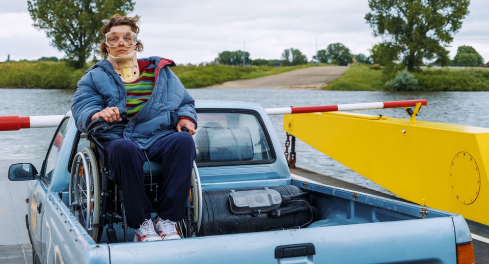 Een jongen in een rolstoel op een auto die op een pont staat