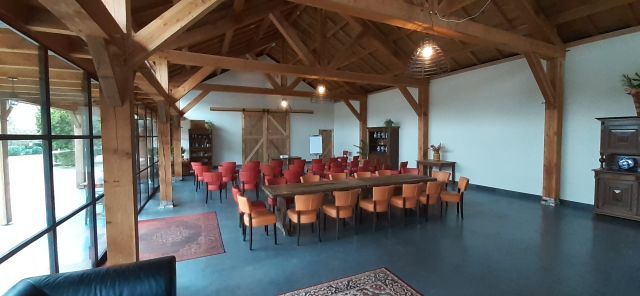 Zaal met houten balken en spanten in het zicht, met tafels en stoelen.