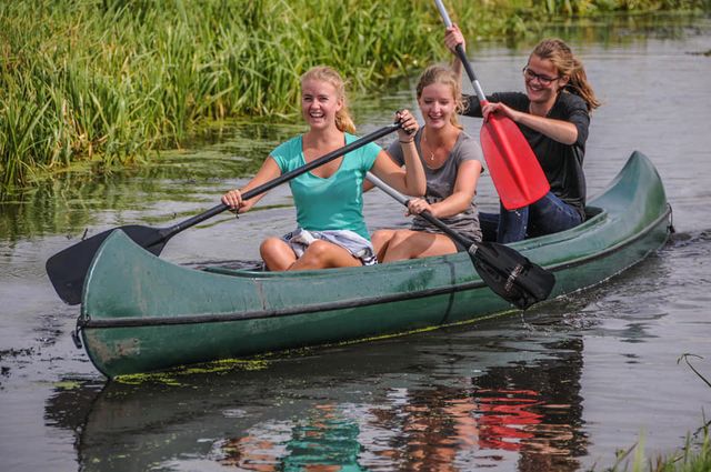 Drie vriendinnen kanoën lachend door een smal watertje tussen het riet bij Boerderij de Boerinn in het Groene Hart.