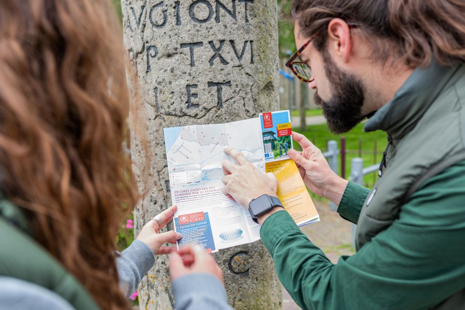 Twee jonge mensen bekijken een kaart van de Limes tegen een replica van een mijlpaal aan.