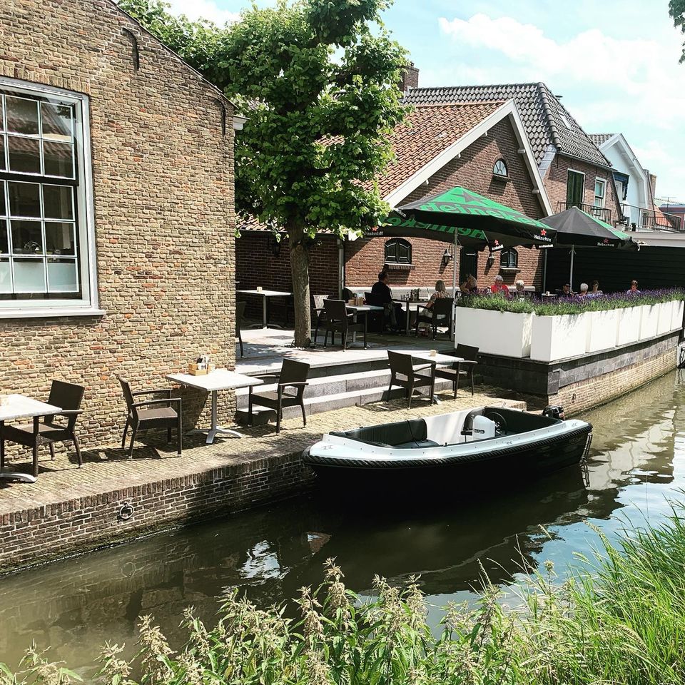 Terras van restaurant Malou Fine Food & Drinks aan het water met zitplaatsen langs de gracht en een bootje aangemeerd.