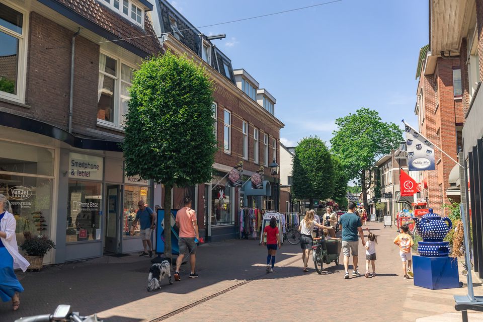 Mensen die door de winkelstraat van Vorstelijk Baarn lopen. Een gezin loopt met kinderen en heeft fietsen in de hand.