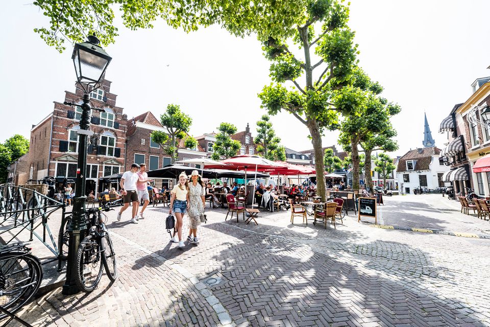 Stadsplein historische binnenstad, Oudewater, Utrechtse Waarden, Groene Hart, levendig plein met terrassen, wandelaars, fietsen en karakteristieke gevels onder gesnoeide lindebomen op een zonnige dag.