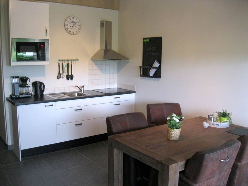 Vakantiehuisje met een wit keukenblok en een eettafel met vier stoelen.