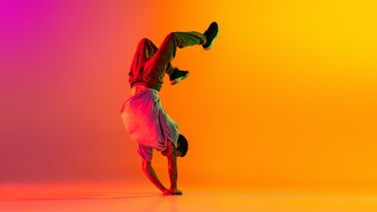 Breakdancer in handstand pose op felgekleurde oranje en roze achtergrond tijdens urban dansoptreden.