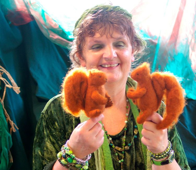 Marleen Groenland in een groene jurk met veel groene kralenkettingen en 2 poppen in de vorm van eekhoorns.