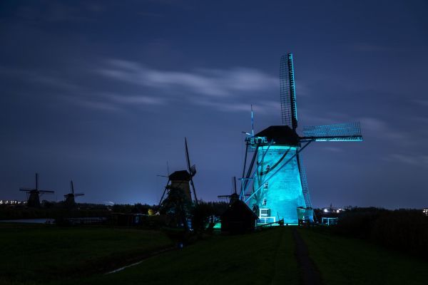 Een molen is blauw uitgelicht in een donkere nacht.