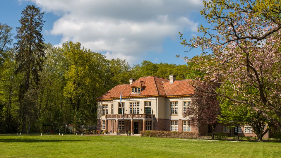Het imposante Verenigingsgebouw uit 1922 tussen hoge groene bomen met een indrukwekkende lucht