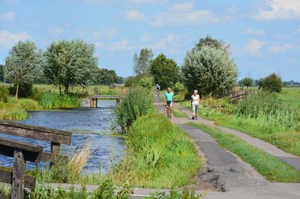 Wandelaars op een smal polderpad langs het water in de Krimpenerwaard, omringd door groen en het open landschap van het Groene Hart.