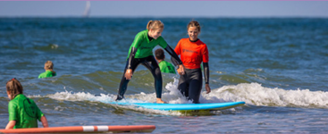 Een kind en ouder die in de zee aan het golfsurfen zijn in een wetsuit