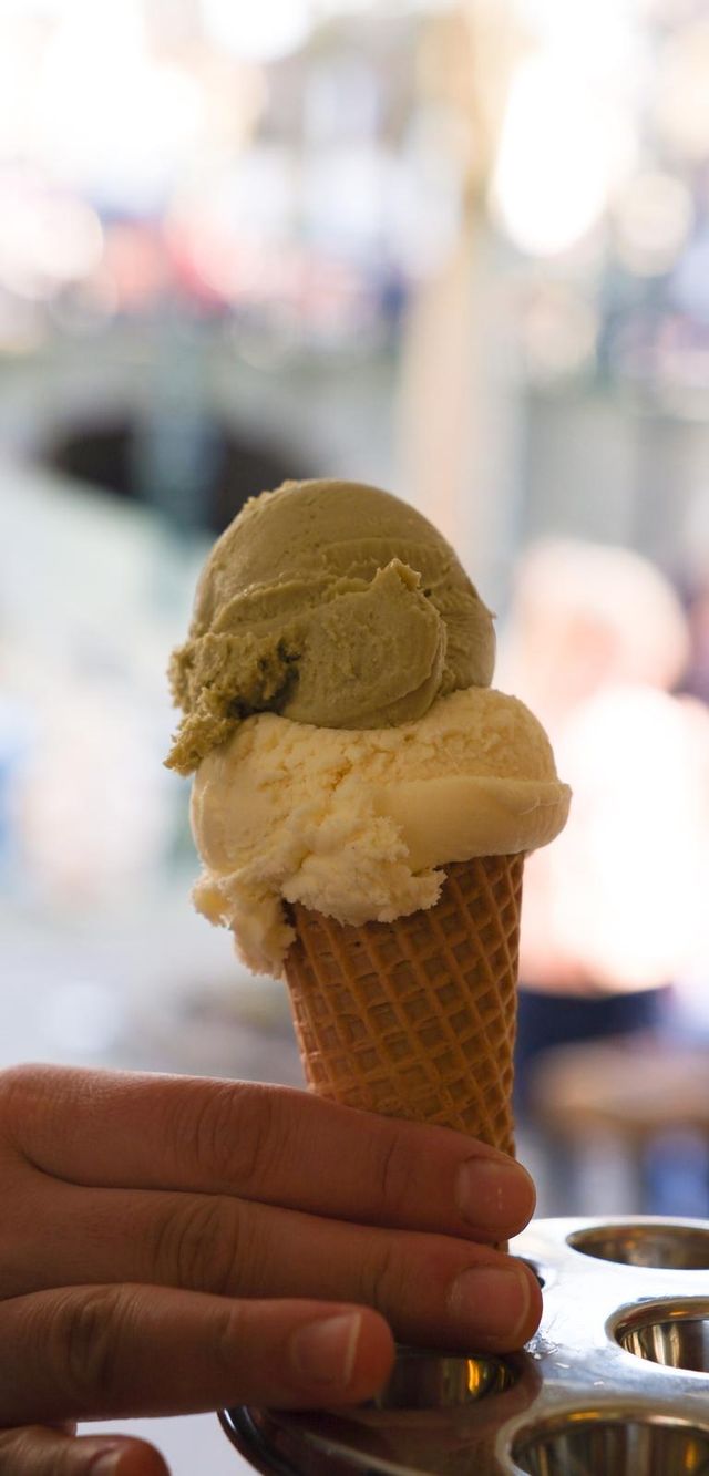 Hoorntje met twee bolletjes ijs (onderop wit en bovenop groen), neergezet in de ijshouder op de toonbank.