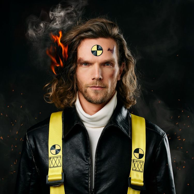 Gezicht van Ruud Smulders. Hij heeft een witte coltrui en een zwart jack met gele banden over de schouders aan. Langs zijn haren zijn vlammen te zien waardoor het lijkt of zijn haren in brand staat.