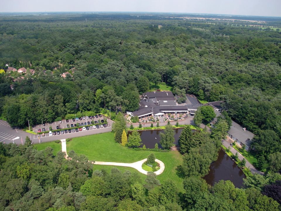 Luchtfoto van de bossen met in het midden een groot grasveld en het hotel-restaurant.