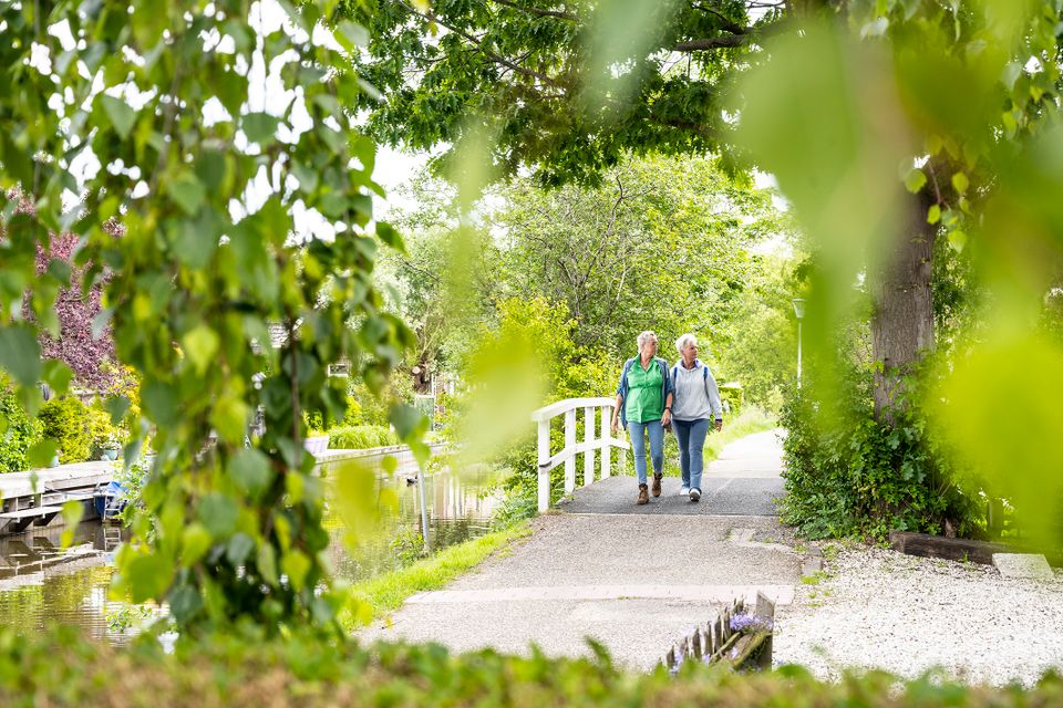 Twee wandelaars door het dorp Linschoten bij een wit bruggetje omgeven door groen.