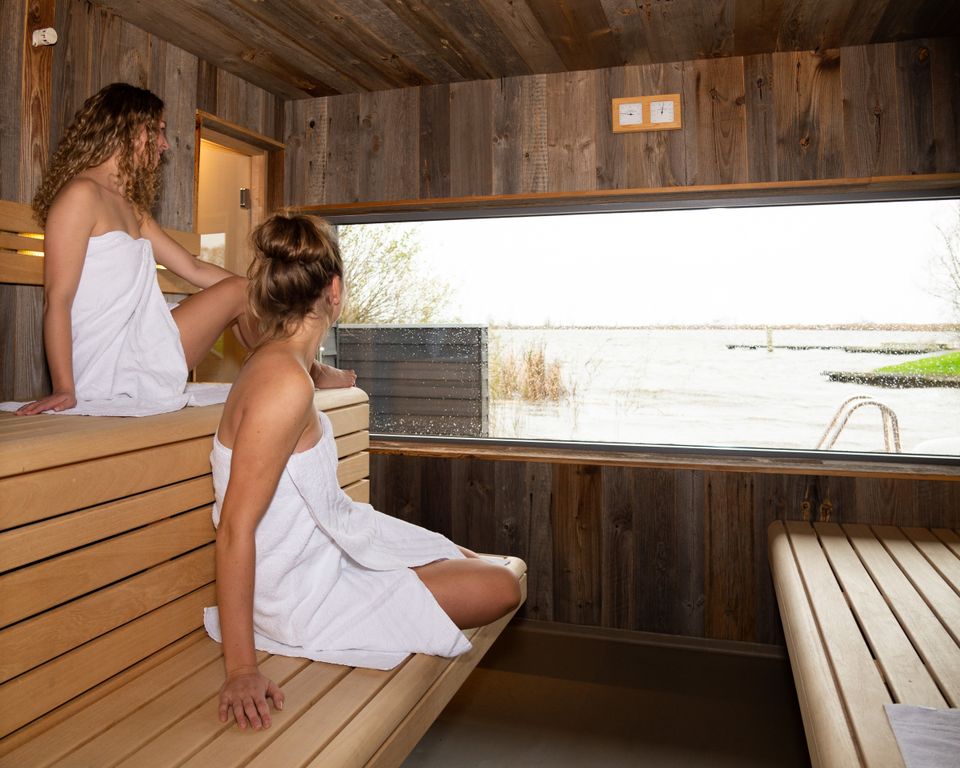 Twee vrouwen in handdoeken gewikkeld in een sauna met uitzicht op het water bij De Pollepleats in Westhem.