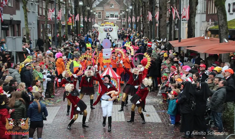 Een carnavalsgroep loopt door de Dorpsstraat tijdens de optocht in Oisterwijk. Er staan veel mensen verkleed langs de kant te kijken.