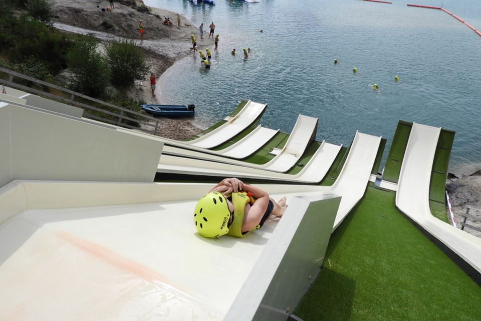 Iemand glijdt met zwemvest aan en helm op van een hele hoge en steile glijbaan het water in.