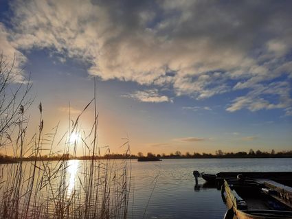 Natuurgebied Reeuwijkse Plassen bij Reeuwijk, Groene Hart, zonsondergang boven het water met riet in de voorgrond en aangemeerde bootjes langs een steiger in een Hollands veenplassengebied.
