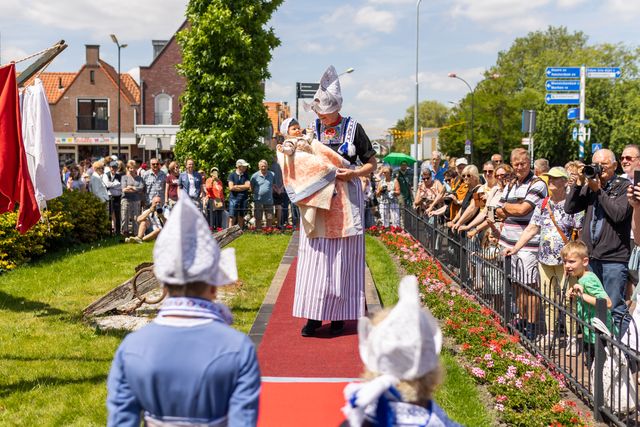 Een vrouw en een baby die in Volendamse klederdracht over de rode loper lopen