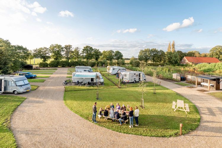 Luchtfoto met blauwe lucht, groenstroken met campers en picknickplekken en een ruim gravel pad.