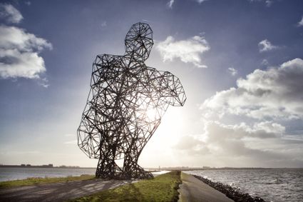 Een enorm hurkende ijzeren man, een 26 meter hoge stalen reus, tuurt eeuwig vanuit de Bataviahaven in Lelystad, op de grens van land en water, richting het Markemeer, een knap staaltje techniek. Met zijn verschijning lokt hij je al van veraf. Hij lijkt zich in een andere, nieuwsgierig makende dimensie te begeven met de steeds veranderende Hollandse luchten als decor.