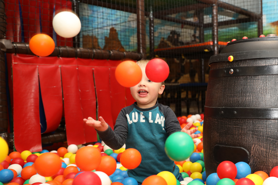 Een jongetje zit in een ballenbak en gooit ballen in de lucht.