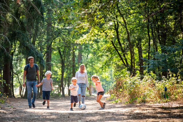 Een familie wandelt en voetbalt in het bos.