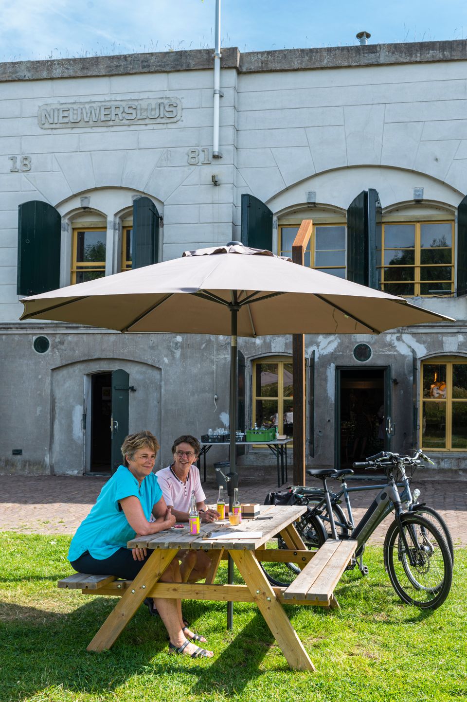 Een man en een vrouw zitten samen op een terras voor een bakstenen fort. Naast hen staan twee fietsen.