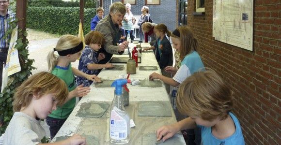 Kinderworkshop bij het museum: kinderen zitten onder een afdak te werken