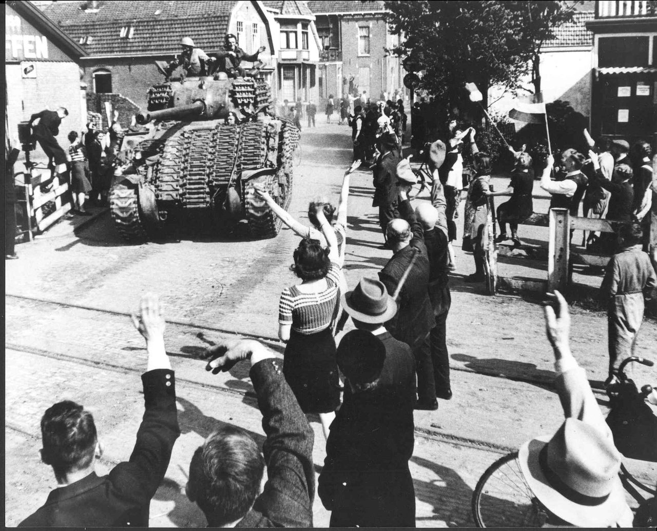 Historische foto tank door straat met zwaaiende mensen ernaast