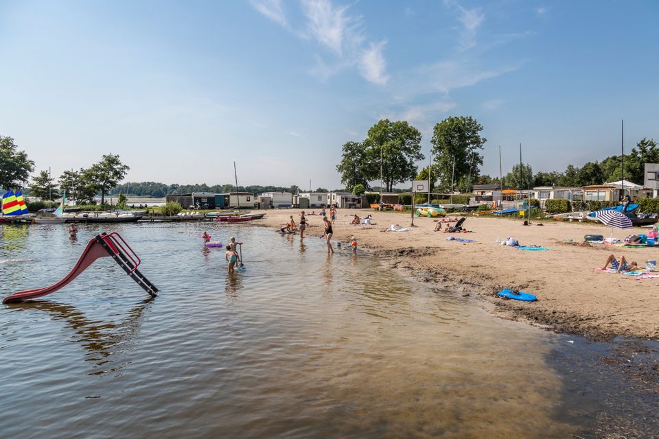 Een foto van het strand aan het nannewiid meer nabij Heerenveen, je ziet veel spelende kinderen en zon.