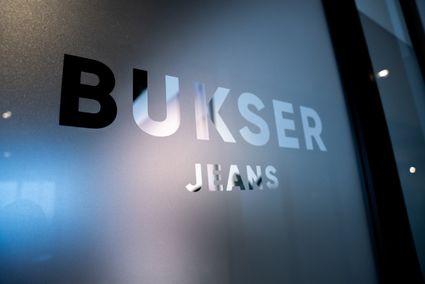Jeanswinkel Busker Jeans in Woerden, Groene Hart, close-up van het logo op een glazen wand als herkenbaar detail van het winkelinterieur.