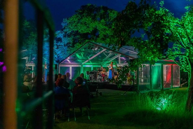 Festival Veenhuizen een sfeervol beeld van een concert in de avond. De tent waarin gespeeld wordt, is prachtig verlicht.