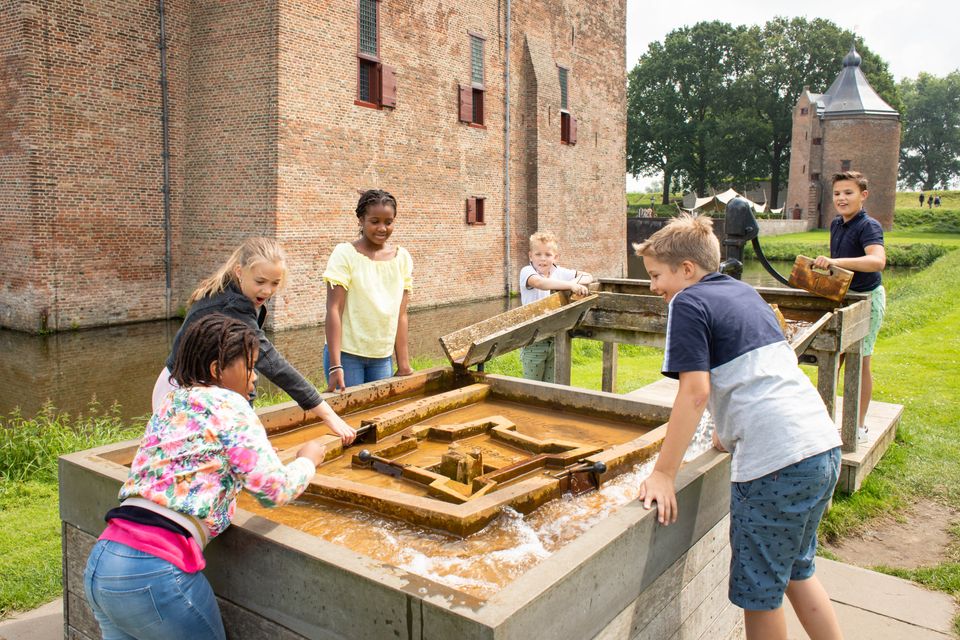 Een groep kinderen speelt een spel in een waterbak voor in een kasteeltuin.