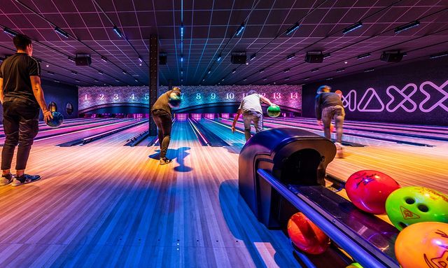 Mensen aan het bowlen in een binnenzaal. de zaal is kleurrijk verlicht en op de voorgrond liggen bowlingballen.