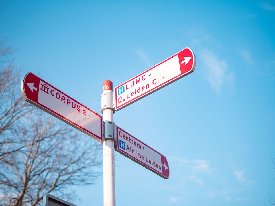 Drie wegwijs bordjes geven de richting naar het LUMC, Corpus, en Leiden Centrum aan.