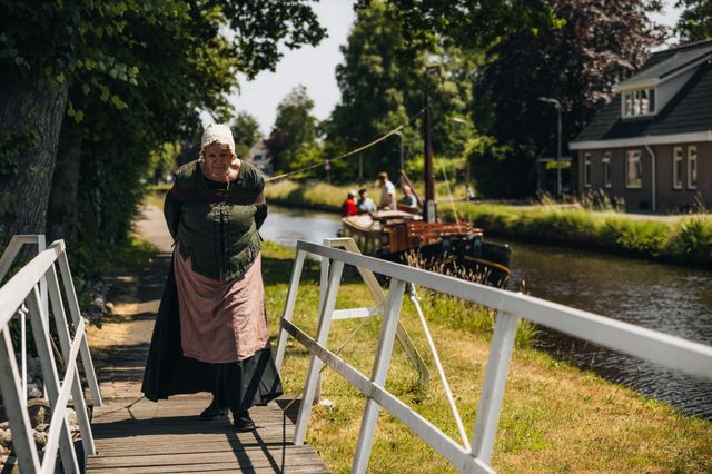 Een vrouw in traditionele kleding trekt een trekschuit voort over een kanaal bij Hoogeveen.
