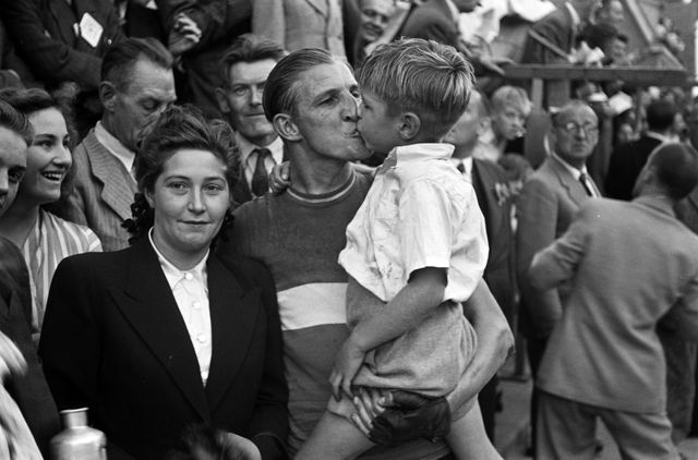 innaar van de Ronde van Oss, Gerrit Schulte, geeft zijn zoontje een zoen om zijn overwinning te vieren. Naast hem staat zijn vrouw Toos v.d. Kleij (1947). Bekijk in beeldbank Historisch Informatie Centrum Oss.