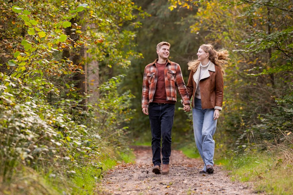 Een man en een vrouw wandelen hand in hand door het bos in de herfst.
