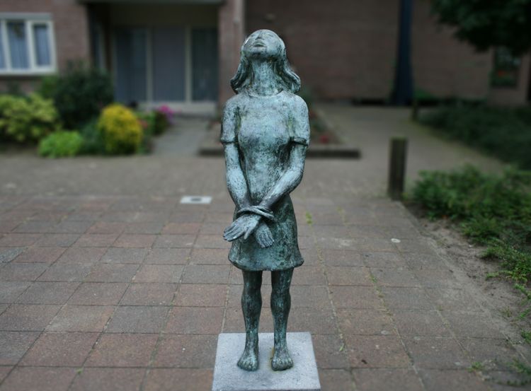 Een beeld in brons van Anne Frank op eren sokkel met haar handen geboeid.