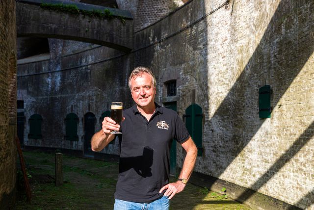 Marco Lauret, ondernemer op Fort Everdingen, staat in de omgang van het bakstenen fort met een glas bier.