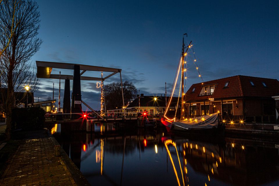 Een winterse foto van gloeiende kerstverlichting aan de zeilen van een aangemeerde zeilboot.