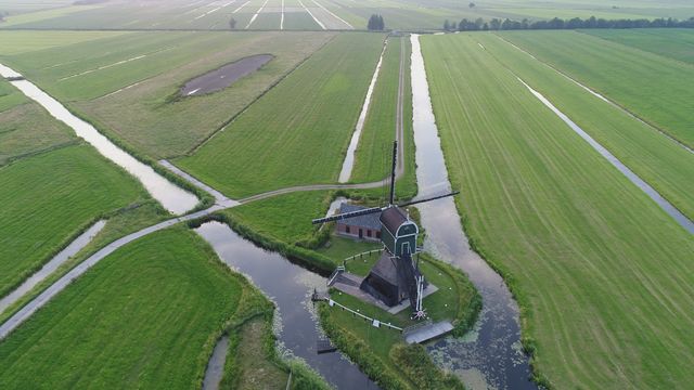 Luchtfoto van de Cabauwse Molen in Lopik: historische poldermolen tussen uitgestrekte groene weilanden en sloten, omgeven door waterlopen en kleine bruggetjes.