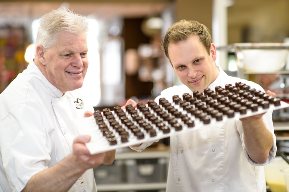 Twee chocolatiers presenteren een blad met tientallen vers gemaakte chocoladebonbons.