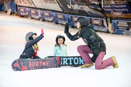 Een foto van een vrouw met twee kinderen. De kinderen hebben gesnowboard en de moeder geeft een high five aan een van de kinderen.