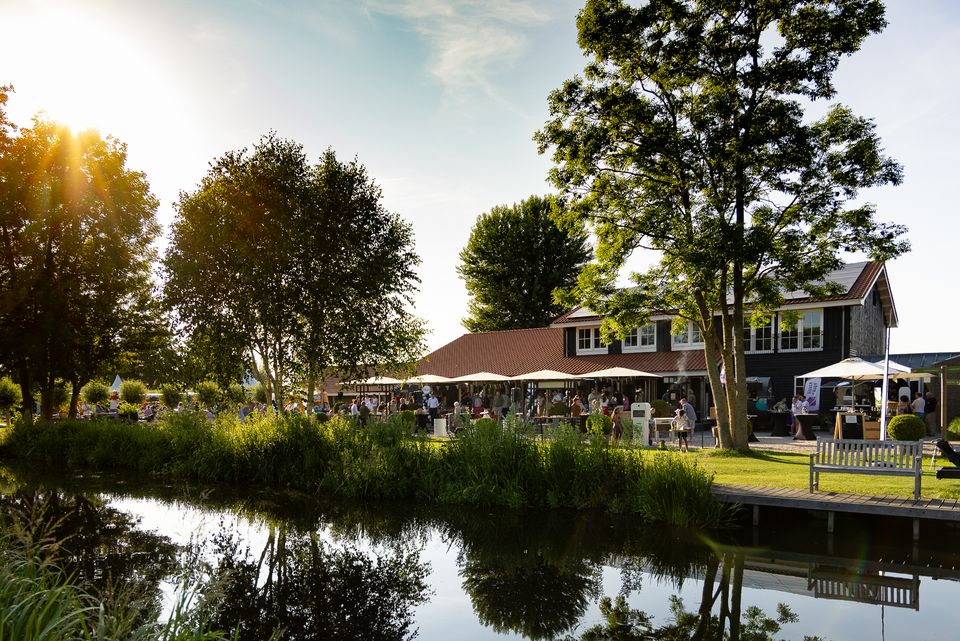 Zonnige terras­sfeer bij Buitenplaats Kameryck in het Groene Hart, met gasten genietend aan het water tussen groene bomen en landelijke natuur – ideale locatie voor evenementen, feesten en buitenactiviteiten.