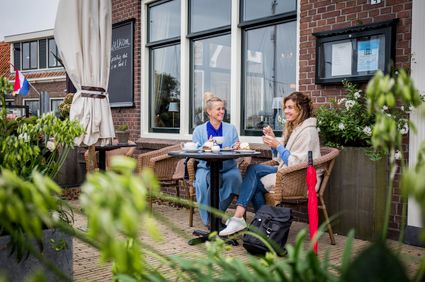 twee vrouwen drinken iets op een terras met gebak erbij