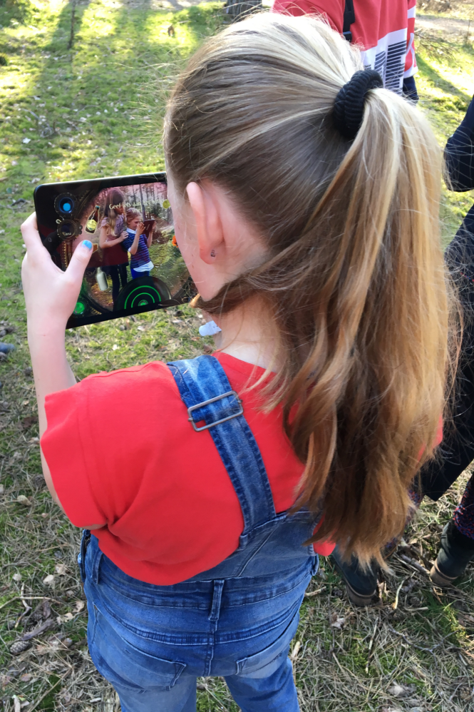 Meisje staat in de natuur met een tablet waarop ze The Nature Game speelt.